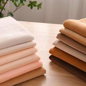 May include: Two separate stacks of folded fabric pieces in various shades of beige, tan, cream, and brown. The left stack features lighter, warmer tones, while the right stack displays a gradient of deeper, earth-toned brown and tan colours.