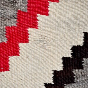 May include: Close-up of a woven rug with a geometric pattern in shades of red, white, black, and gray.