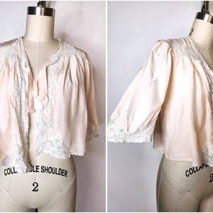 May include: A pale pink satin robe with lace trim and a bow at the neckline. The robe is on a dress form.