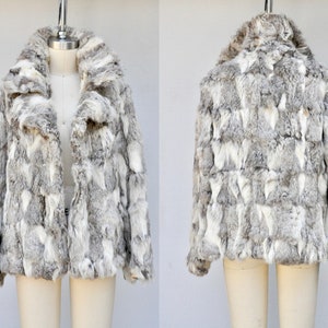 May include: A grey and white faux fur jacket with a collar. The jacket is made of a soft, plush fabric and has a zip closure.