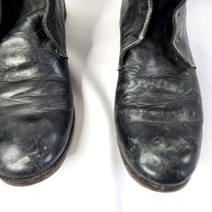 May include: Close-up of a pair of black leather boots with white stitching. The boots have a worn and distressed look.