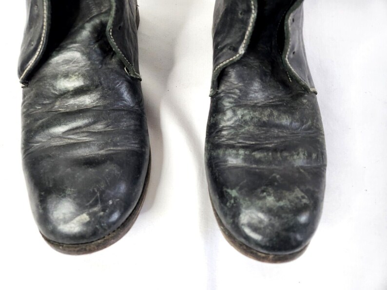 May include: Close-up of a pair of black leather boots with white stitching. The boots have a worn and distressed look.