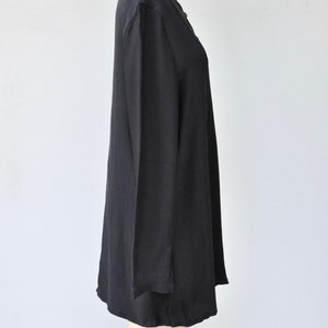 May include: A black long-sleeved tunic top with a V-neckline. The top is made of a soft, flowing fabric and has a relaxed fit.
