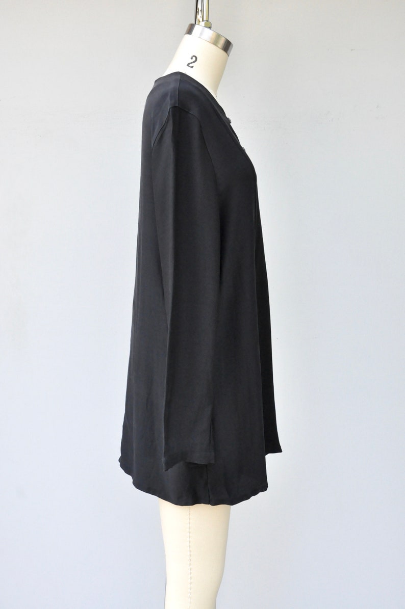 May include: A black long-sleeved tunic top with a V-neckline. The top is made of a soft, flowing fabric and has a relaxed fit.