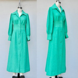 May include: A long-sleeved, green dress with a button-up front and a white trim around the collar, cuffs, and waist. The dress has a slightly flared skirt and is made of a textured fabric.