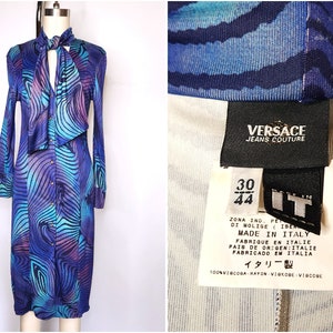 May include: A blue and purple long-sleeved dress with a swirling pattern and a bow tie. The dress has a button-up front and is made by Versace Jeans Couture. The tag says "Made in Italy" and lists the size as 30/44.
