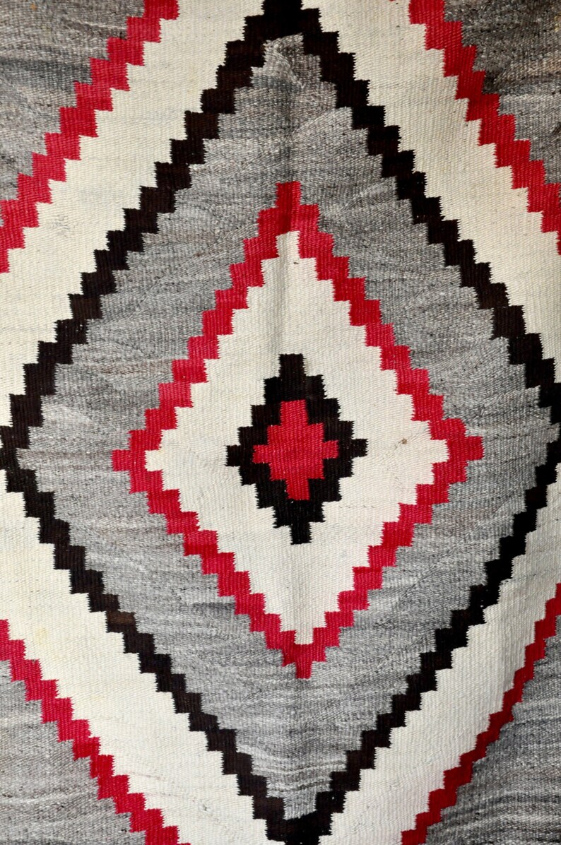 May include: A Navajo rug with a geometric pattern in red, black, and white. The rug is woven with a traditional design.