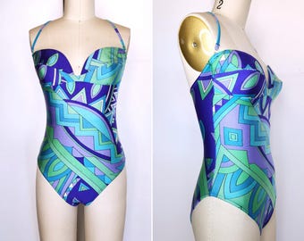 May include: A vintage one-piece swimsuit with a vibrant geometric pattern in shades of blue, green, and purple. The swimsuit features a sweetheart neckline, halter straps, and a high-cut leg design. The swimsuit is displayed on a mannequin.