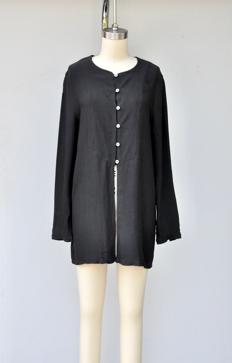 May include: A black long-sleeved shirt with a button-up front and a long slit in the back.