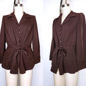 Puede incluir: Una camisa marrón de manga larga con botones, cinturón de lazo y parte delantera plisada.