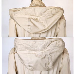 May include: A beige hooded jacket with a zipper closure and a button on the hood. The jacket has a pocket on the hood.