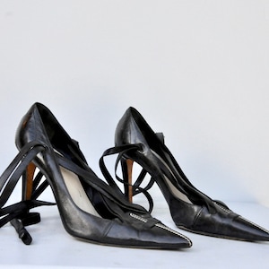 May include: A pair of black leather high-heeled shoes with pointed toes and black ribbon laces.