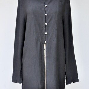 May include: A long-sleeved black button-up shirt with a center front slit. The shirt has a round neckline and a relaxed fit.