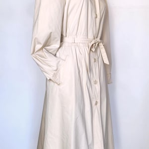 May include: A long-sleeved, cream-colored hooded jacket with a button-up front and a tie belt. The jacket has a relaxed fit and a slightly flared skirt.