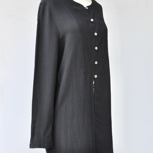 May include: A black long-sleeved button-up shirt with a round neckline. The shirt is made of a smooth, silky fabric and has a slightly loose fit.