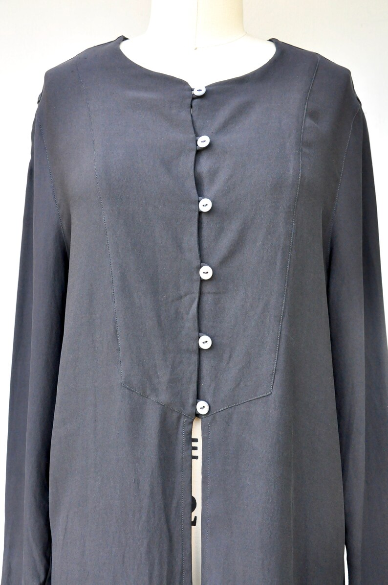 May include: A long-sleeved black button-up shirt with a center front opening. The shirt has a simple, classic design and is made of a lightweight fabric.