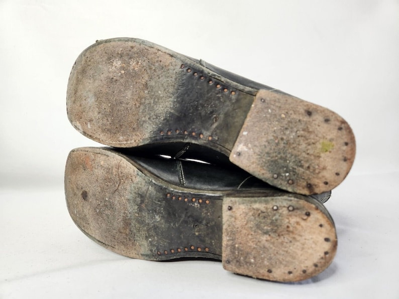 May include: Close-up of the soles of a pair of black leather boots. The soles are worn and have a pattern of small, round studs.