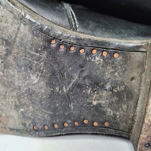 May include: Close-up of the bottom of a black leather boot with a row of copper rivets along the edge.