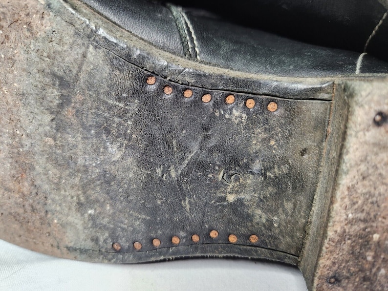 May include: Close-up of the bottom of a black leather boot with a row of copper rivets along the edge.