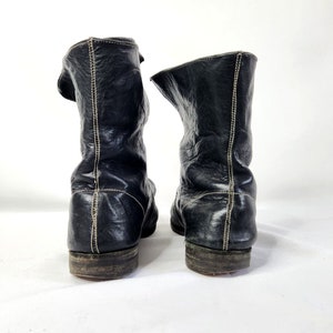 May include: A pair of black leather boots with a pointed toe and a zipper on the side. The boots have a stitched seam down the back of the shaft.