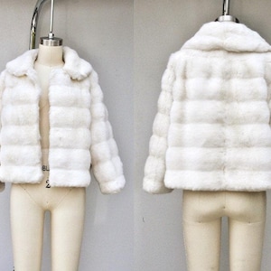 May include: A white faux fur jacket with a collar and long sleeves. The jacket is made of soft, fluffy material and has a slightly cropped length.