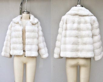 May include: A white faux fur jacket with a collar and long sleeves. The jacket is made of soft, fluffy material and has a slightly cropped length.