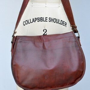 Może przedstawiać: Brązowa sk&oacute;rzana torba na ramię z długim, regulowanym paskiem. Pasek jest oznaczony napisem "COLLAPSIBLE SHOULDER 2".