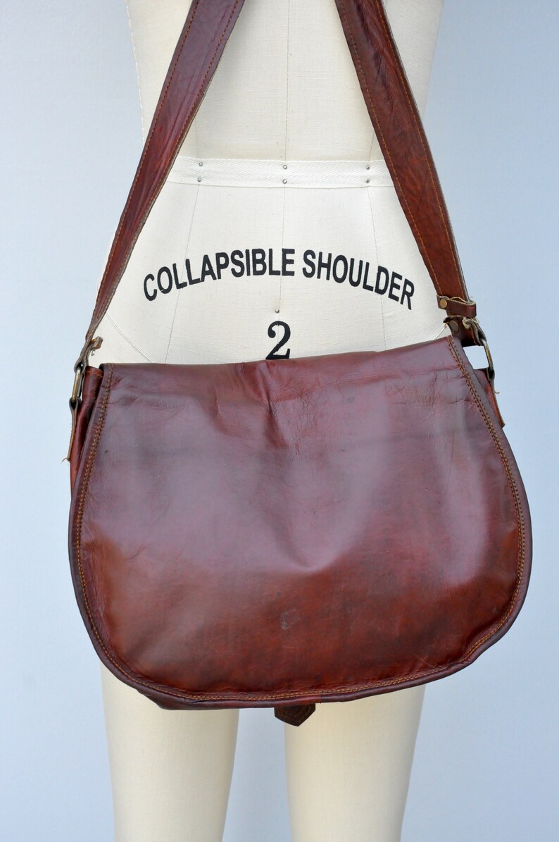 Może przedstawiać: Brązowa sk&oacute;rzana torba na ramię z długim, regulowanym paskiem. Pasek jest oznaczony napisem "COLLAPSIBLE SHOULDER 2".
