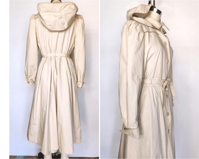 May include: A long, white, hooded raincoat with a drawstring waist and a button-up front. The raincoat has a relaxed fit and a slightly flared skirt.