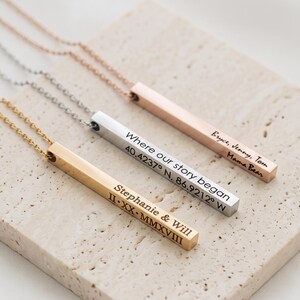 Puede incluir: Tres collares de barra de metal en tonos oro, plata y oro rosa. Cada barra está grabada con texto personalizado: 'Stephanie & Will II-XX-MMXVIII', 'Where our story began 40.4237° N, 86.9212° W' y 'Bryce, Jenny, Tom Mama Bear'.