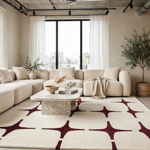 Puede incluir: Una alfombra rectangular con una base de color crema y un patrón repetitivo de formas de estrella de cuatro puntas en color burdeos oscuro. La alfombra está colocada en una sala de estar bajo una mesa de centro de piedra y un sofá modular.