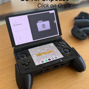 Może przedstawiać: Czarna przenośna konsola do gier AYN THOR LO-KII GripCase z dwoma ekranami. Górny ekran pokazuje folder All Games, a dolny ekran wyświetla menu gry. Widoczny jest tekst AYN THOR LO-KII GripCase Click on Grips.