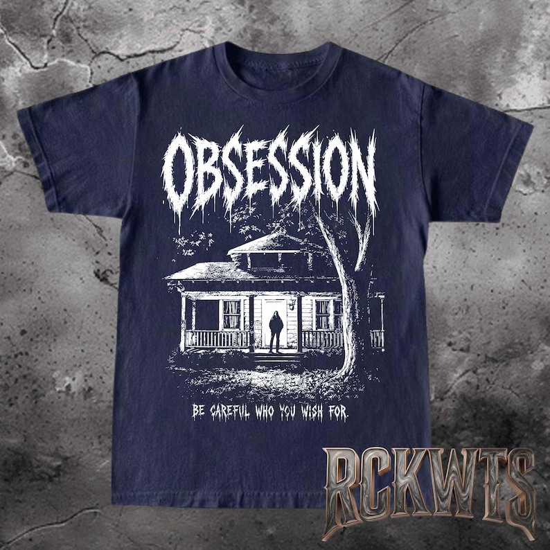 May include: A dark navy blue t-shirt featuring a white graphic print of a house with a person standing in the doorway. The word OBSESSION is printed in a jagged, dripping font above the house, and the text BE CAREFUL WHO YOU WISH FOR is below.