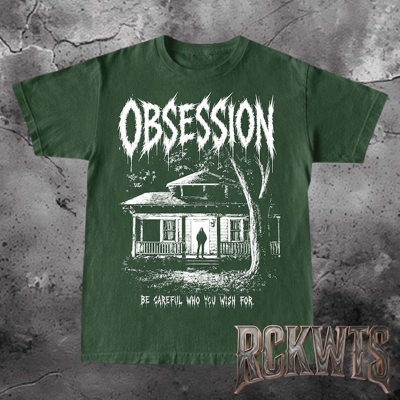 May include: A dark forest green short-sleeve t-shirt featuring a white graphic print of a house with a figure standing in the doorway. The word OBSESSION is printed in a jagged font above, and the text BE CAREFUL WHO YOU WISH FOR is below.