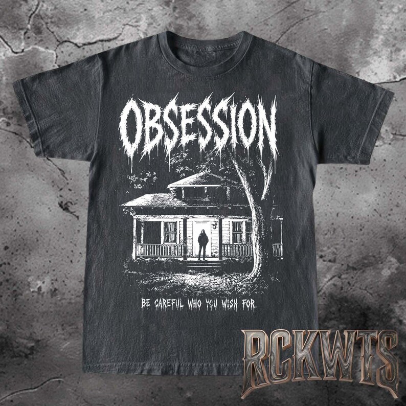 May include: A black short-sleeved t-shirt featuring a white graphic print of a house with a figure standing in the doorway. The word OBSESSION is printed in a jagged font above the house, and the text BE CAREFUL WHO YOU WISH FOR is below.