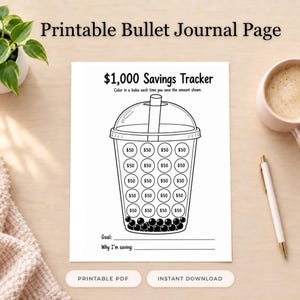 Può includere: Una pagina di diario puntinato stampabile con un tracker di risparmio da 1.000 $ e un'illustrazione di una tazza di tè boba. La tazza contiene venti cerchi etichettati con 50 $ da colorare, con righe in basso per un obiettivo e la motivazione.