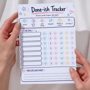 May include: A white paper Done-ish Tracker task list with colorful icons and text. The header reads Done-ish Tracker and Because partial progress still counts. It includes seven numbered rows with columns for status icons like hearts, stars, and clocks.