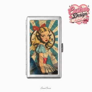 May include: A rectangular silver metal cigarette case featuring a vintage-style illustration of a blonde character with a red hair bow, blue dress, and white apron. The background displays a teal and white sunburst pattern with a clock face graphic.