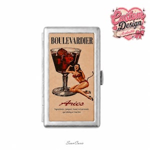 Puede incluir: Una pitillera rectangular de metal plateado con un gráfico de estilo vintage de una copa de cóctel etiquetada BOULEVARDIER, una figura diabólica, el texto Aries y los ingredientes Campari, Sweet red vermouth, rye whisky o bourbon.