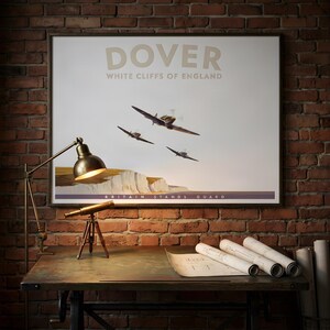 May include: A framed travel poster titled DOVER WHITE CLIFFS OF ENGLAND featuring three vintage propeller airplanes flying over white cliffs. The text at the bottom reads BRITAIN STANDS GUARD. The poster is displayed on a brick wall.