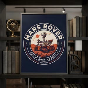 May include: A framed rectangular print featuring a circular emblem with a dark blue background. The graphic depicts a Mars rover on a rocky red landscape with the text MARS ROVER, RED PLANET ROBOTICS, and EST. 1976 in white lettering.