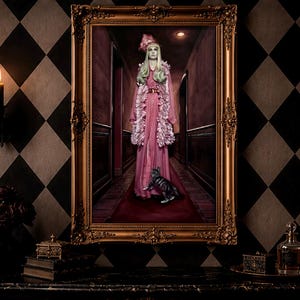May include: A rectangular wall art piece in an ornate gold frame depicting a person with long light hair wearing a pink ruffled gown and a matching hat, standing in a dark hallway with a small cat. The scene features a red carpet and dim lighting.