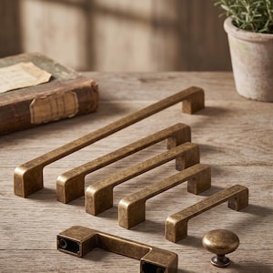 May include: A collection of antique brass cabinet hardware including five rectangular bar pulls of varying lengths and one round knob. Each piece features a distressed, weathered finish with visible dark brown undertones and a smooth, solid metal construction.