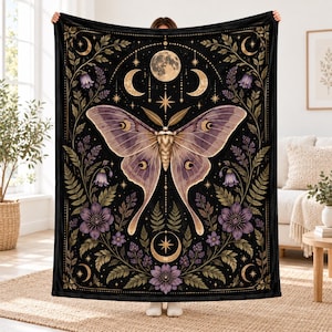 May include: A black rectangular throw blanket featuring a large central moth with light purple wings. The design includes a full moon, crescent moons, stars, and purple flowers with green foliage arranged in a symmetrical botanical pattern.