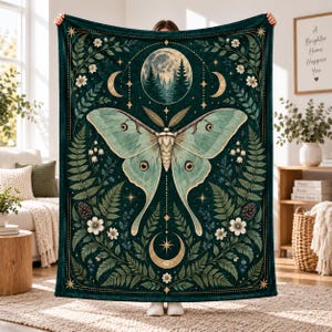 Puede incluir: Una manta rectangular de color verde oscuro con una gran polilla de color verde pálido en el centro. El diseño incluye una luna llena con pinos, lunas crecientes, estrellas, frondas de helecho, piñas y flores blancas en un patrón simétrico.