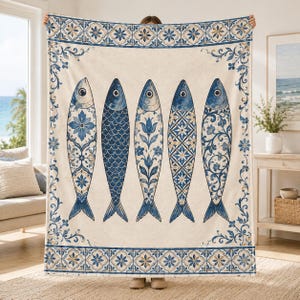 May include: A large rectangular throw blanket featuring a cream-colored background with a repeating blue and gold tile-style border. The center displays five vertical fish illustrations, each decorated with distinct blue and white patterns.