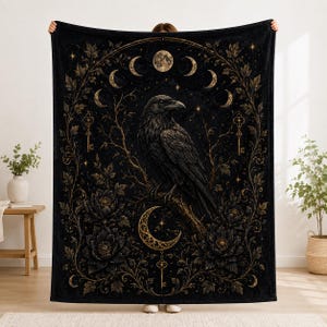Peut inclure: Un plaid noir orné d'un corbeau central perché sur une branche, entouré de motifs floraux dorés, de clés et d'un cycle de phases lunaires. Le design comprend un croissant de lune en bas et une pleine lune en haut, sur un fond sombre.