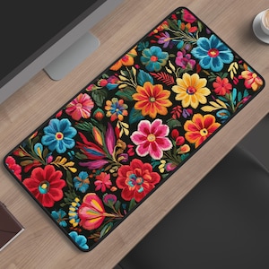 May include: A rectangular desk mat featuring a vibrant, multi-colored floral pattern on a black background. The design includes various stylized flowers in shades of red, pink, yellow, orange, and blue, accented with green leaves and stems.