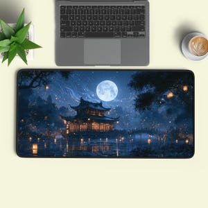 May include: A rectangular desk mat featuring a nighttime scene of a traditional East Asian pavilion illuminated by warm lights, situated by a calm body of water under a large full moon, with floating lanterns and dark trees surrounding the structure.