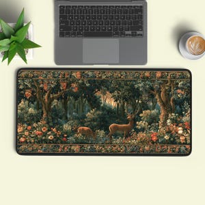 May include: A rectangular desk mat featuring a detailed forest scene with two deer standing among dense trees, lush foliage, and colourful flowers. The design includes small heraldic shields hanging from tree branches and a decorative border.